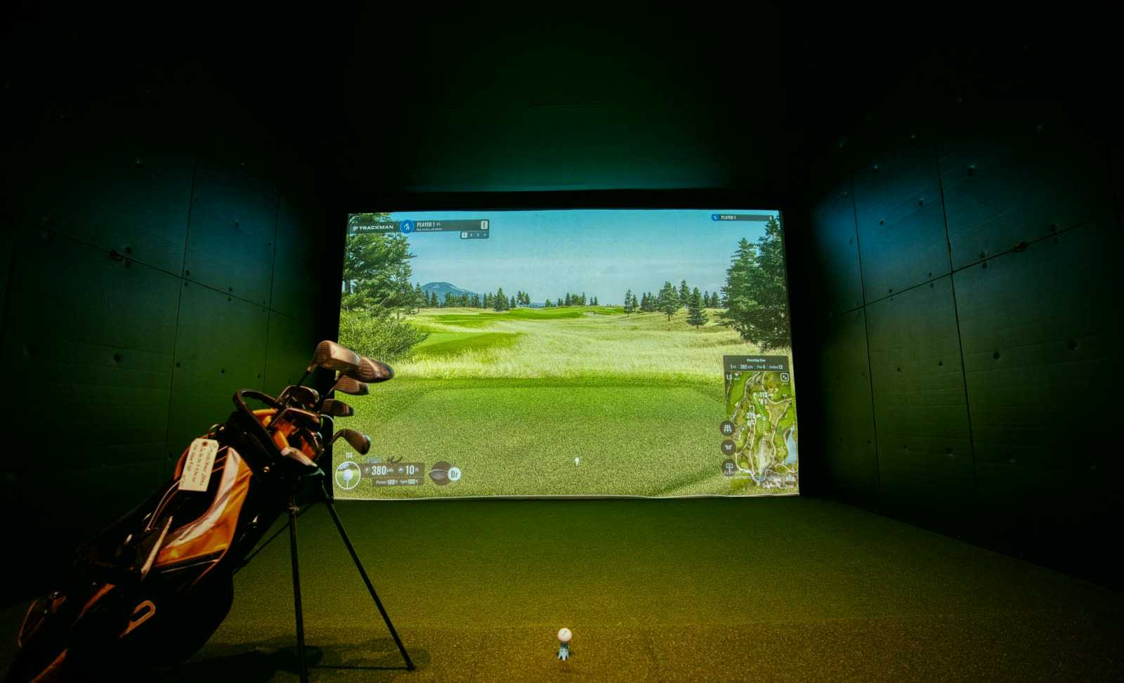 Concept image: a dark indoor golf simulator bay with a lit impact screen